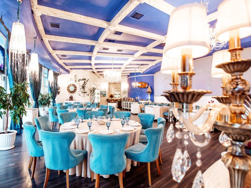 restaurant hall with turquoise chairs navy coloured ceiling classic chandeliers and white walls